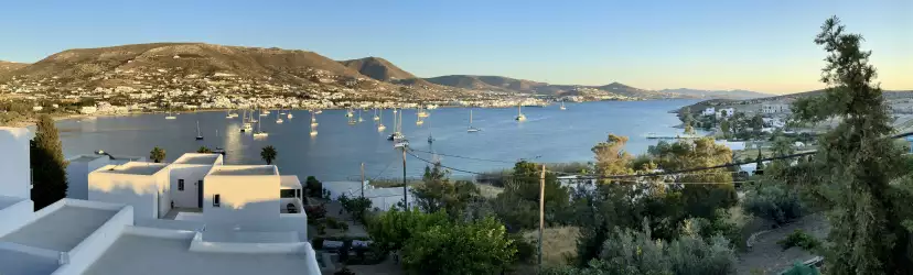 Panoramic view of Parikia bay with white sailing boats moored in the bay, and the town of Parikia laying and the foot of the Marpissa mountains