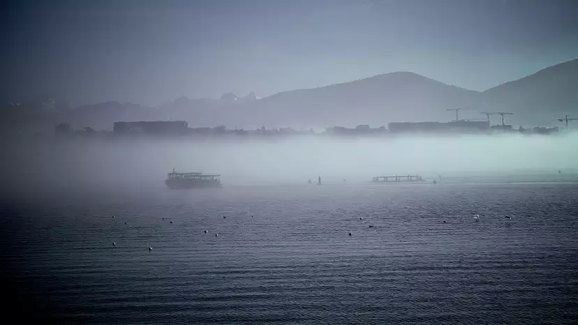 A layer of fog above the lake with a boat shrouded in it