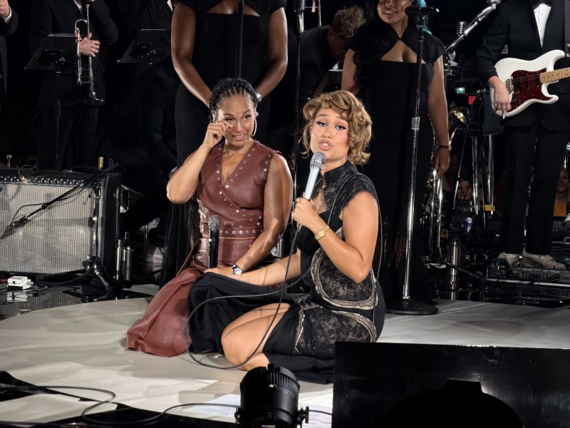 Alicia Keys and RAYE sitting on stage. RAYE's looking in my directions while Alicia wipes a tear.