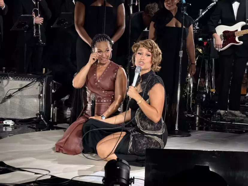 Alicia Keys and RAYE sitting on stage. RAYE's looking in my directions while Alicia wipes a tear.