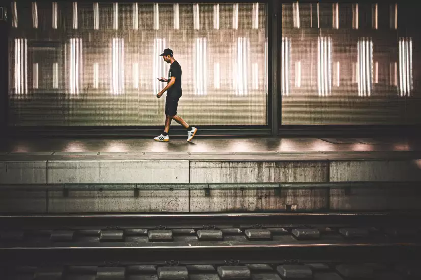 A man looking at his smartphone walking on the opposite plateform
