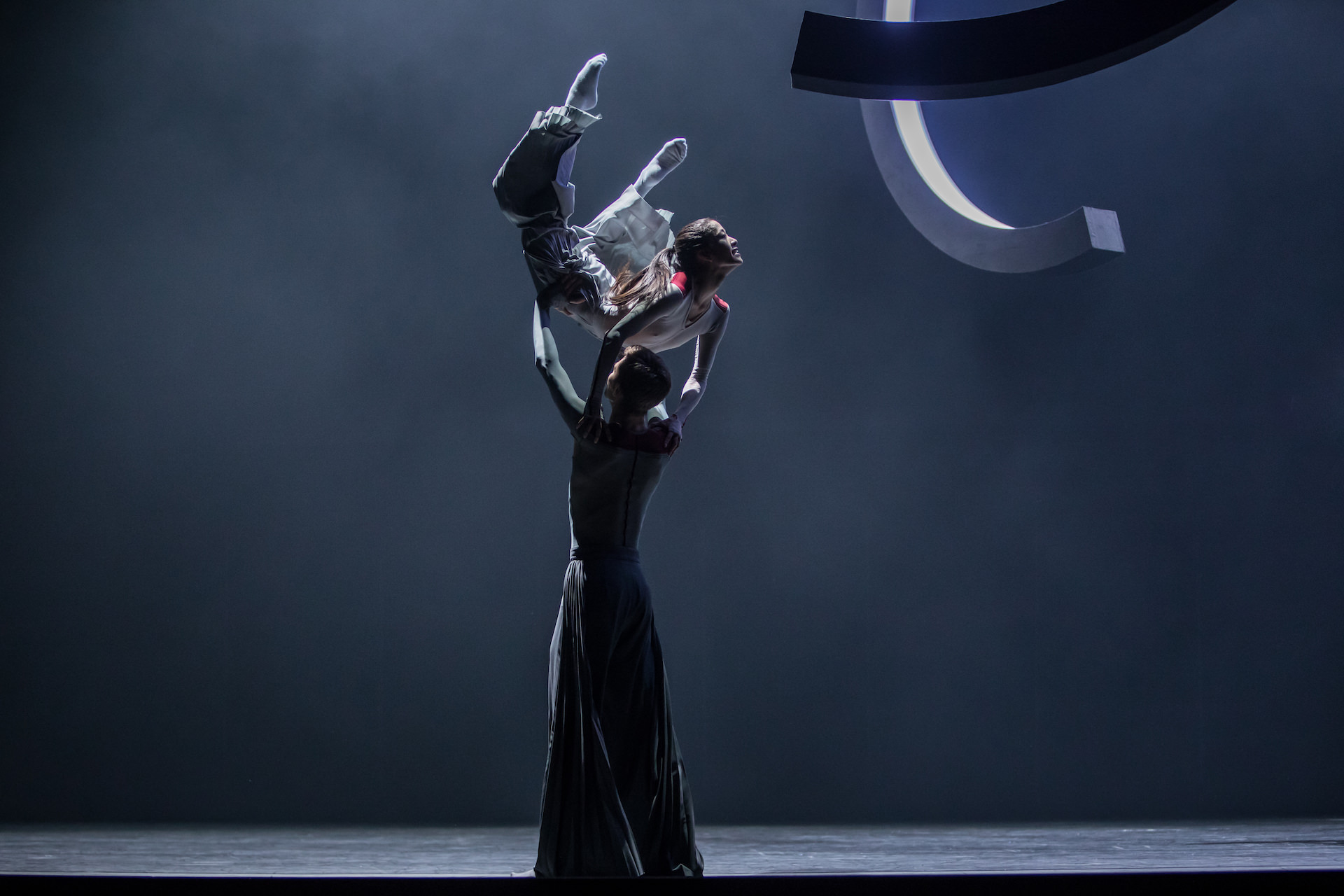 Porté. Male dancer carrying his partner through the stage in a dark grey atmosphere. Photo by Gregory Batardon.