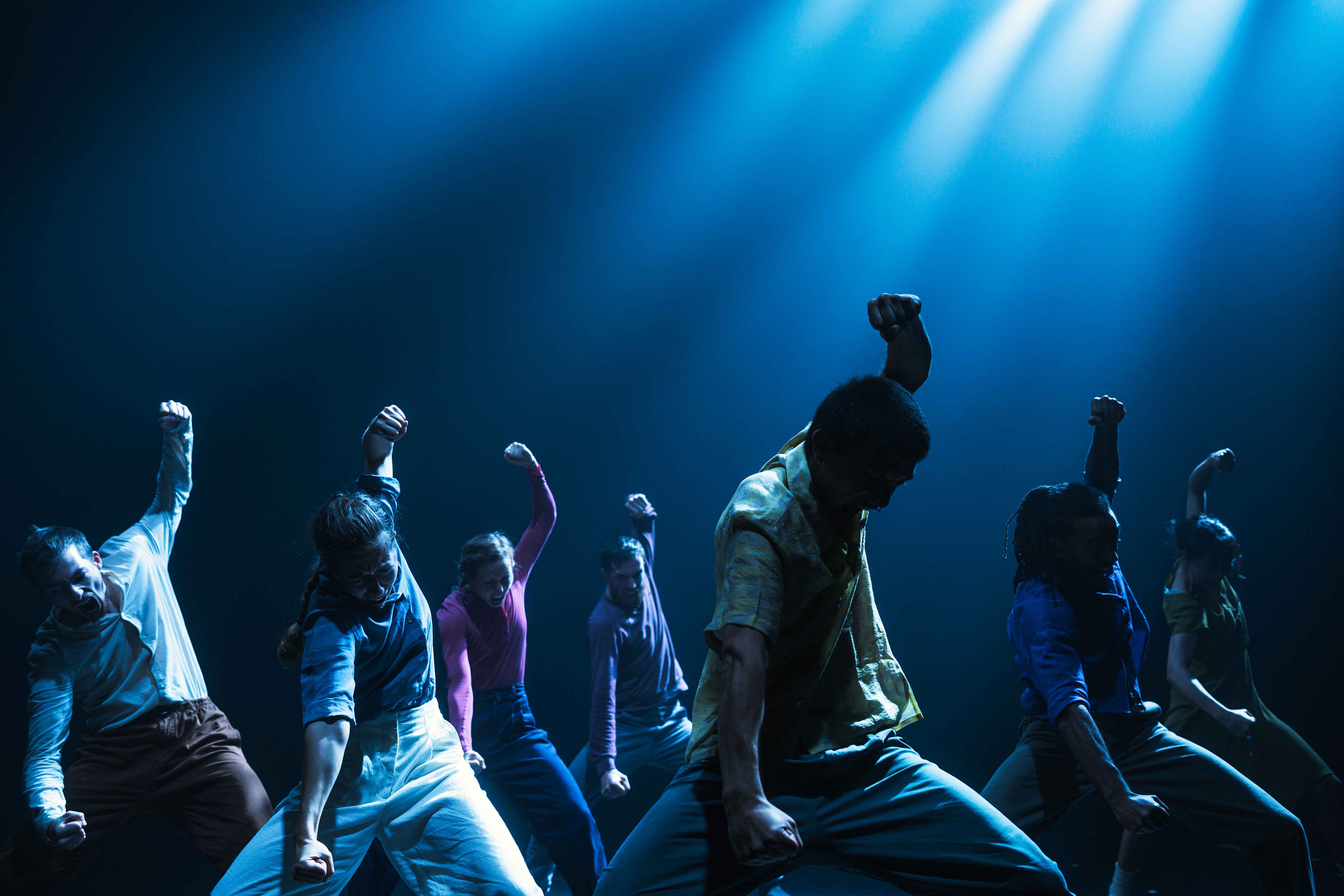 Dancers rising their fists on a blue backdrop © Hofesh Shechter Company