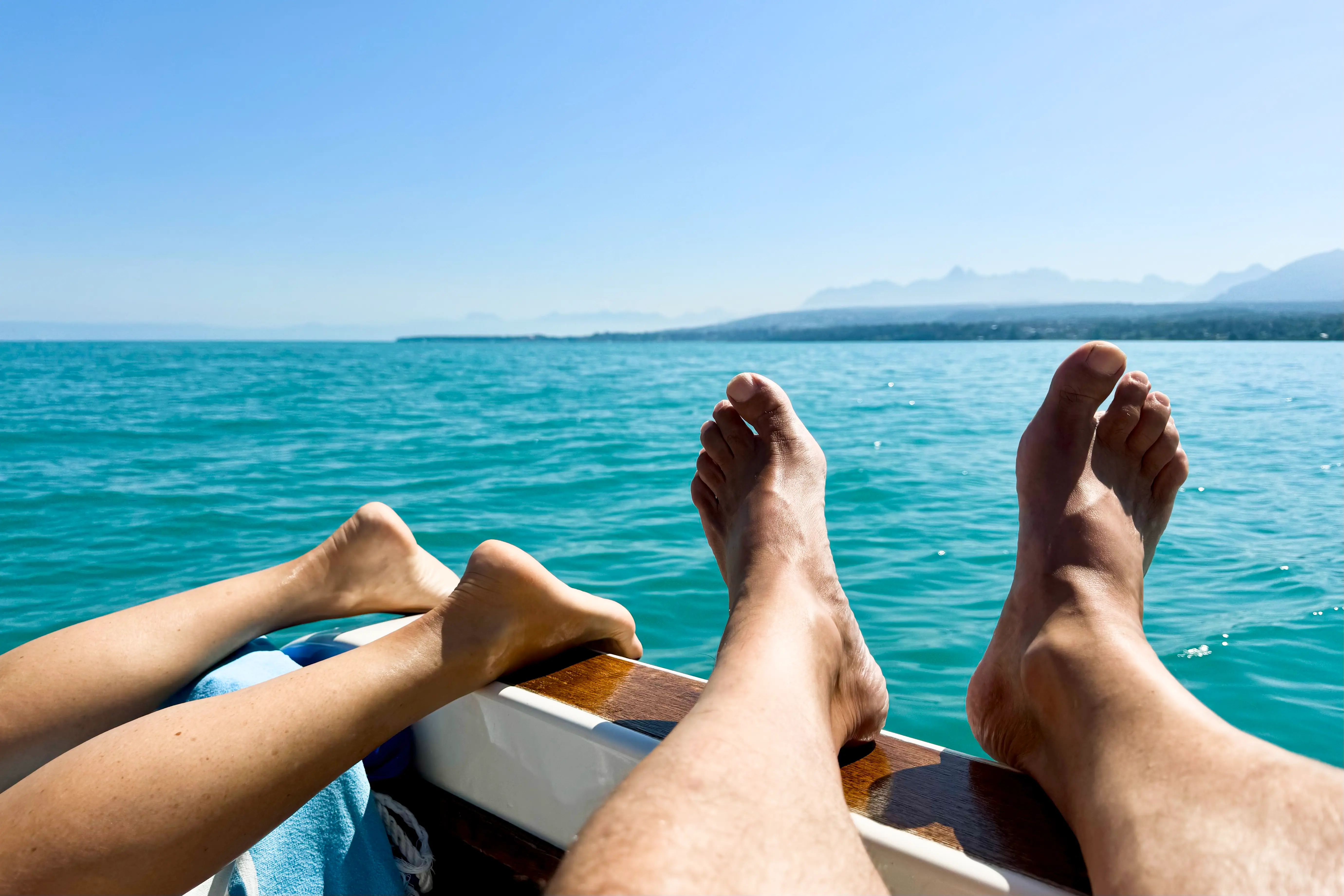 Our feet propped on the side of the boat on and emerald lake under blue skies